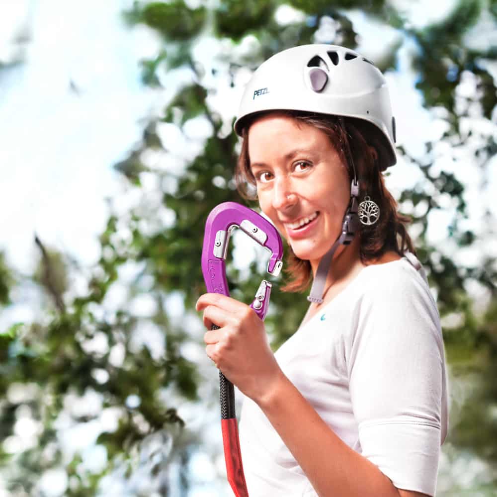 Nahaufnahme einer Frau mit Kletterhelm auf dem Kopf und Kletter-Karabiner in der Hand