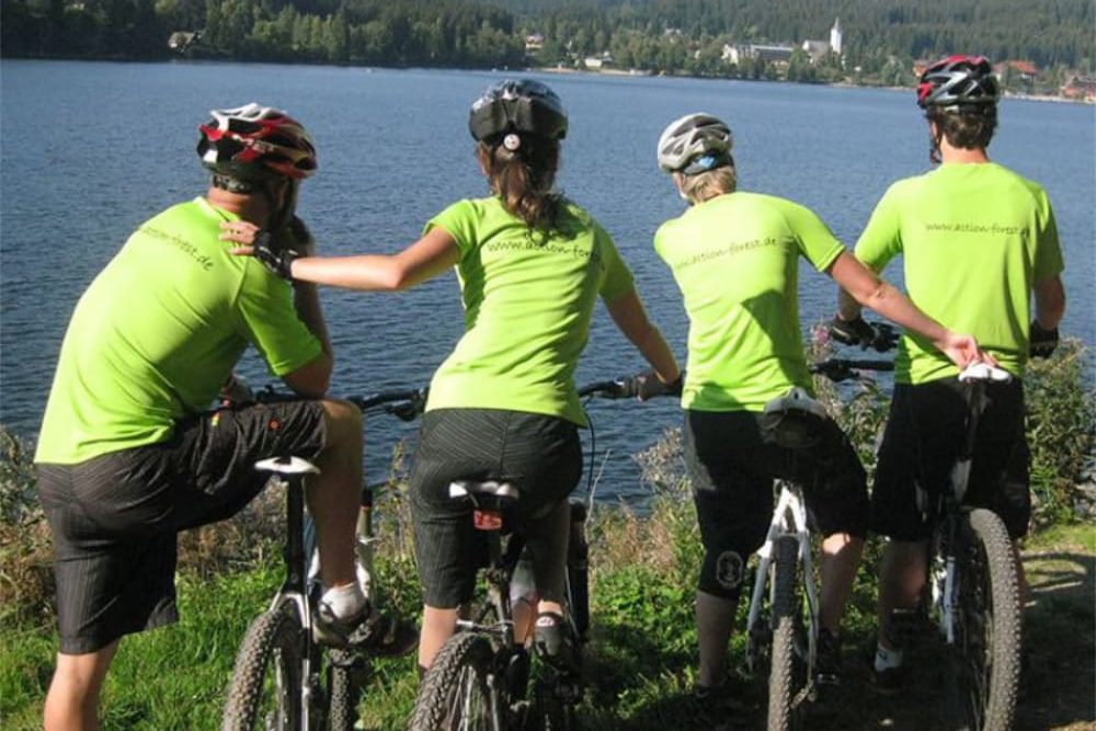 Vier Personen stehen mit ihren Fahrrädern am Ufer des Titisees